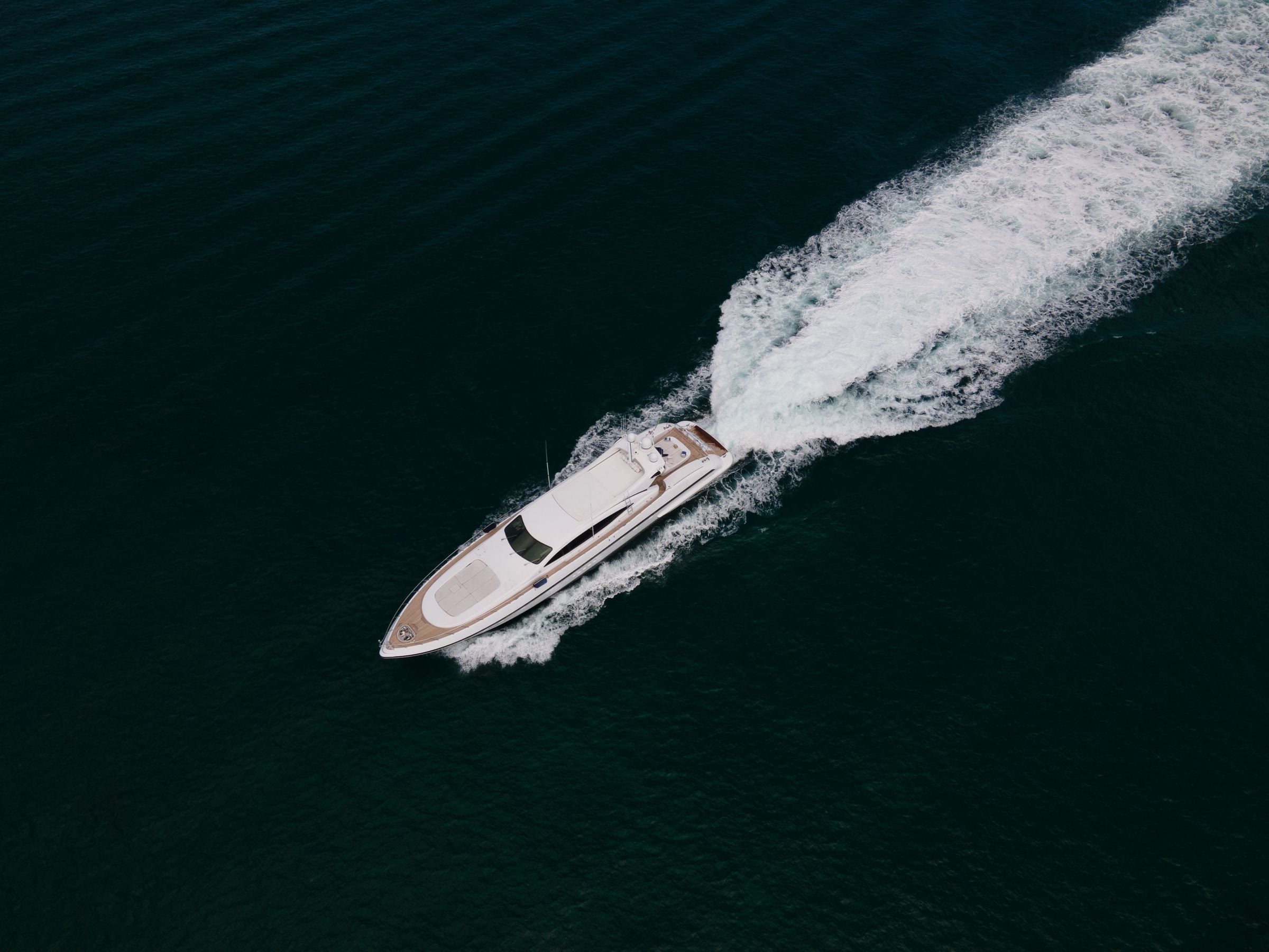 A yacht underway on open water seen from above, a long white wake behind it
